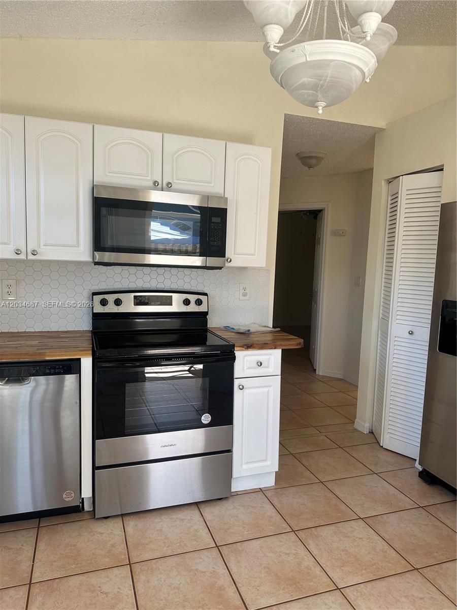 A kitchen features white cabinets, stainless steel appliances, a tiled backsplash, and light-colored floor tiles — 12338 SW 144th Ter, Miami FL 33186, MIAMI, FL