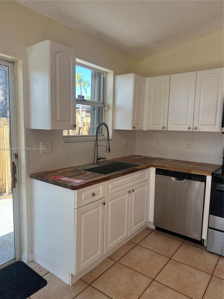 A kitchen features white cabinets, a wood countertop, a stainless steel dishwasher, and tiled flooring — 12338 SW 144th Ter, Miami FL 33186, MIAMI, FL