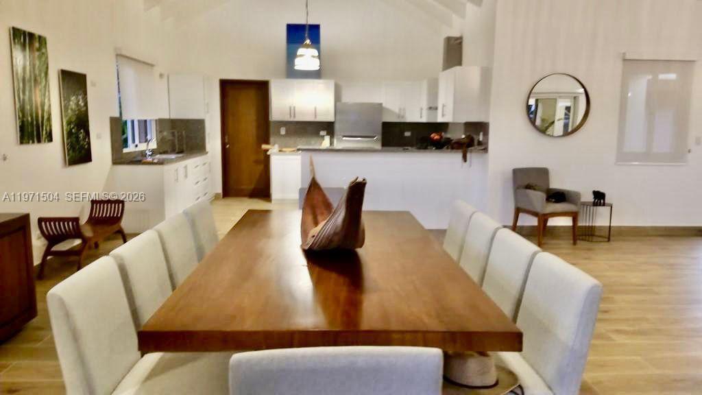 A dining area with a large wooden table and chairs opens into a white kitchen — Samanes, La Estancia Golf & Country Club, DR, DR