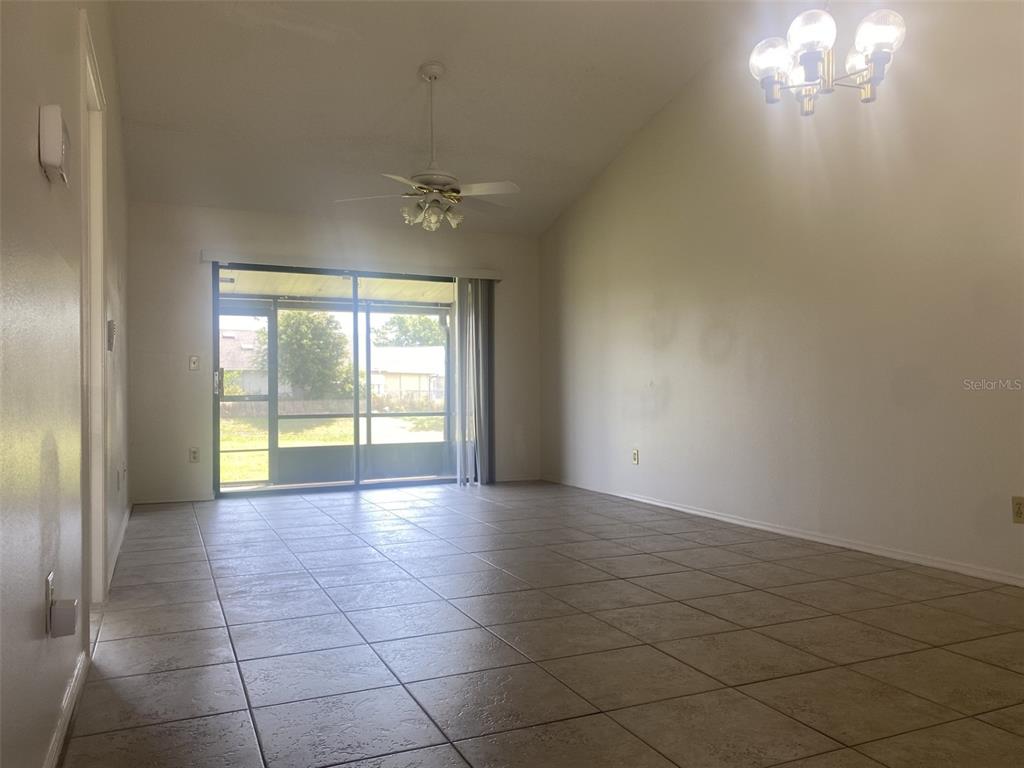 A living room with tile flooring, a vaulted ceiling, a ceiling fan, and sliding glass doors — 42 PINE ISLAND CIRCLE, KISSIMMEE, FL