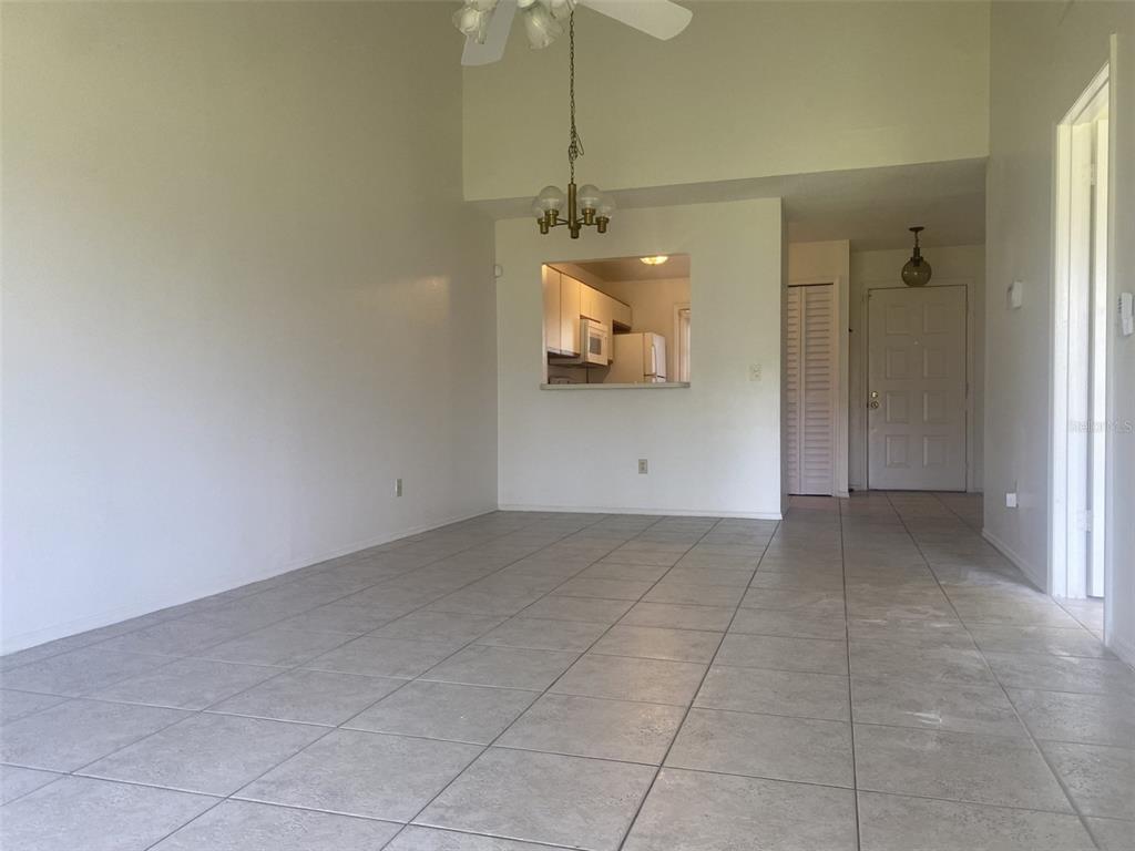 A living room with light tile flooring, a vaulted ceiling, and a kitchen pass-through window — 42 PINE ISLAND CIRCLE, KISSIMMEE, FL