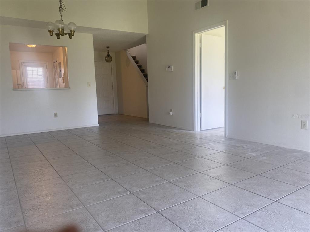A living area features light-colored tile flooring, white walls, a pass-through window, and stairs — 42 PINE ISLAND CIRCLE, KISSIMMEE, FL