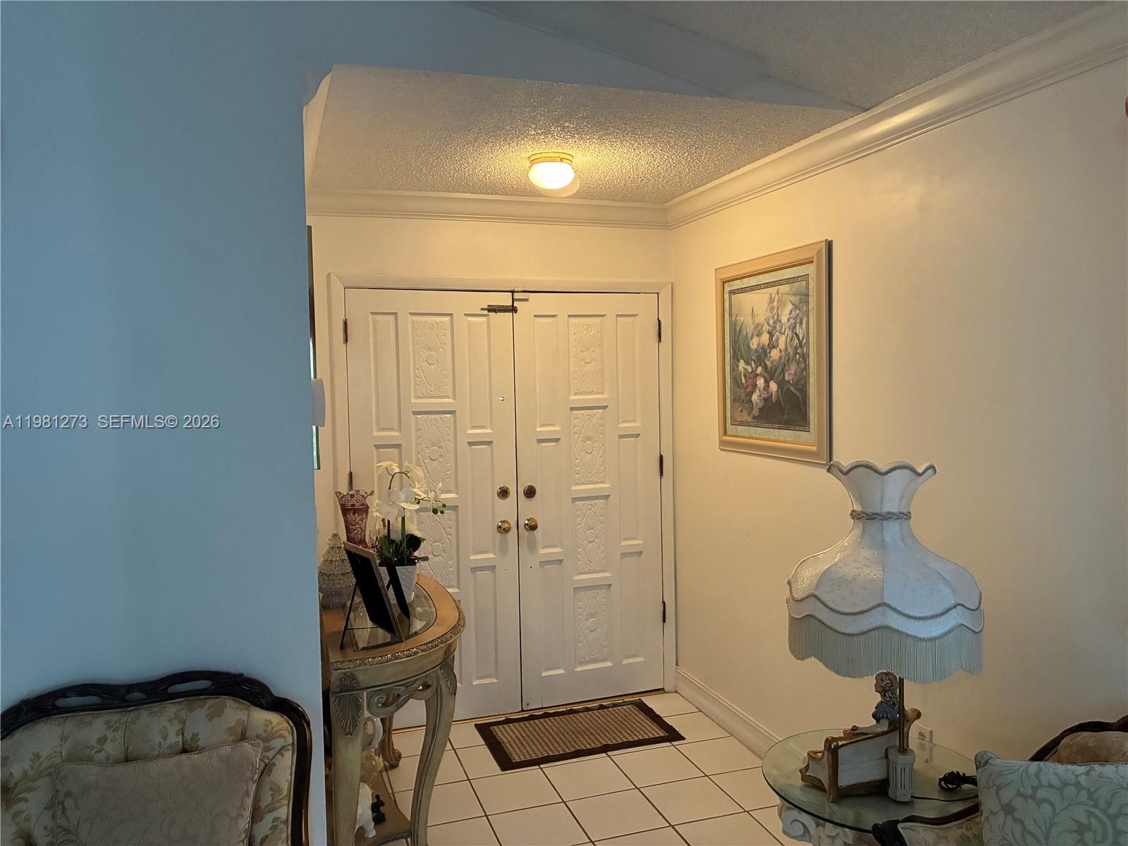 An entryway features double white doors, a tiled floor, and a decorative table with flowers — 18175 NW 61st Ave # 0, Miami FL 33015, MIAMI, FL