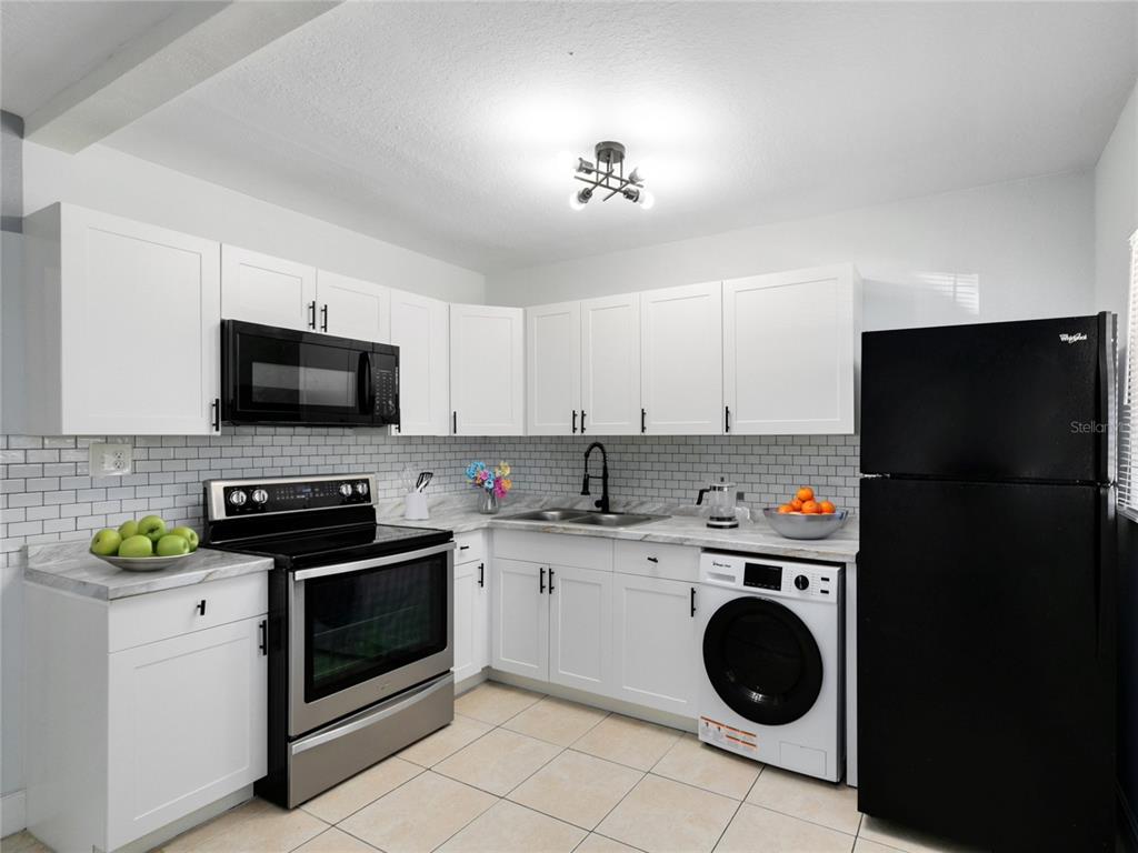 A kitchen features white cabinets, a subway tile backsplash, stainless steel appliances, and a washer — 955 6TH STREET SE UNIT 5, WINTER HAVEN, FL