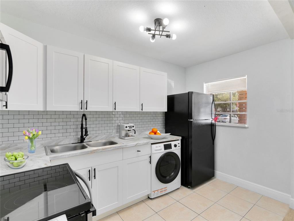 A kitchen with white cabinets, a black refrigerator, a built-in washer, and subway tile backsplash — 955 6TH STREET SE UNIT 5, WINTER HAVEN, FL