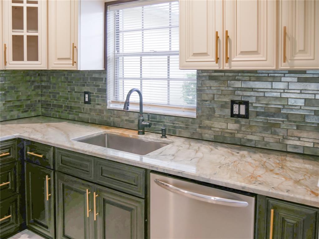 A kitchen features green lower cabinets, cream upper cabinets, a marble countertop, and a tiled backsplash — 2411 ASPINWALL STREET UNIT 2411, SARASOTA, FL