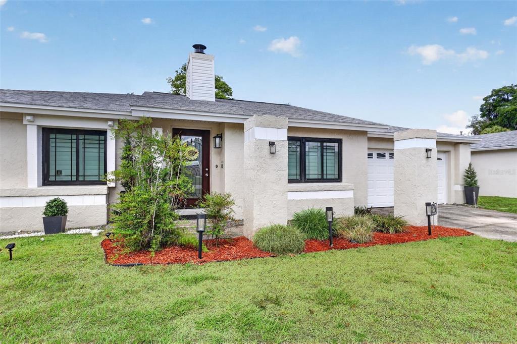 A single-story house with a beige stucco exterior, a chimney, and a front garden bed — 575 TIBERON COVE ROAD, LONGWOOD, FL