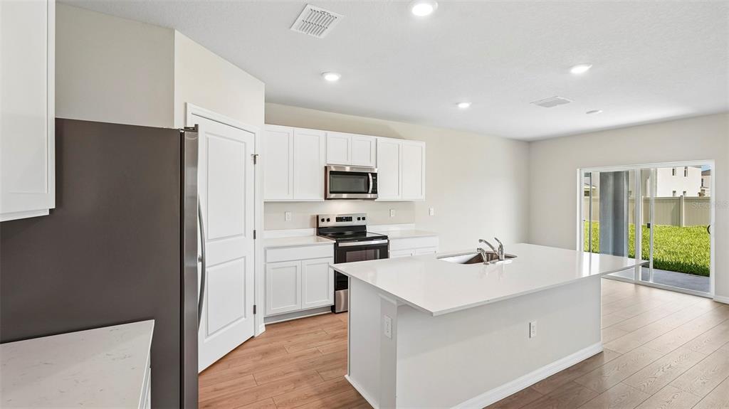 A modern kitchen features white cabinetry, stainless steel appliances, a quartz island, and wood-look flooring — 5423 SILVER MOONLIGHT DRIVE, PALMETTO, FL