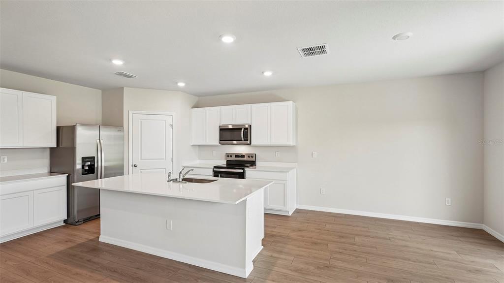 A modern kitchen features white cabinets, stainless steel appliances, a center island, and wood-look flooring — 5423 SILVER MOONLIGHT DRIVE, PALMETTO, FL