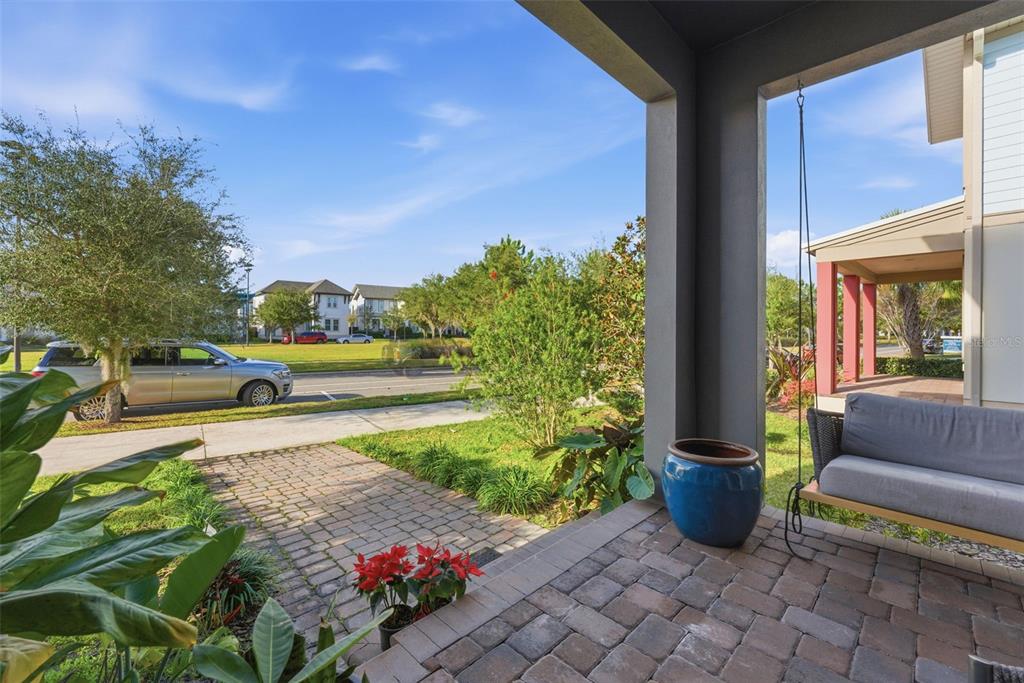 A covered porch features brick pavers, a hanging swing, and a blue decorative planter — 8266 NEMOURS PARKWAY, ORLANDO, FL