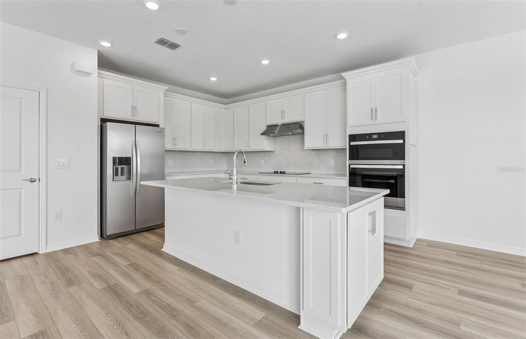 A modern kitchen features white cabinetry, stainless steel appliances, and a large central island — 1294 LAKERIDGE WAY, LAKE ALFRED, FL