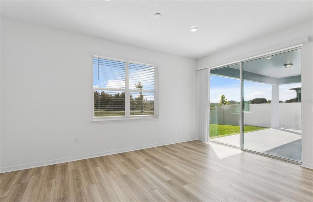 An empty room with light wood-look flooring, a window, and sliding glass doors to a patio — 1294 LAKERIDGE WAY, LAKE ALFRED, FL