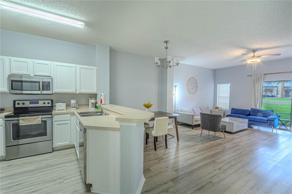 An open-concept kitchen and living area features white cabinets, stainless steel appliances, and wood flooring — 8502 CRYSTAL COVE LOOP, KISSIMMEE, FL