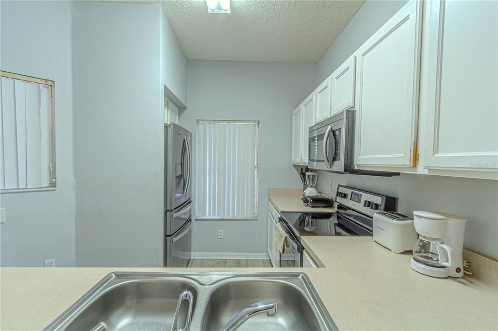 A kitchen features white cabinets, stainless steel appliances, a double sink, and light-colored countertops — 8502 CRYSTAL COVE LOOP, KISSIMMEE, FL