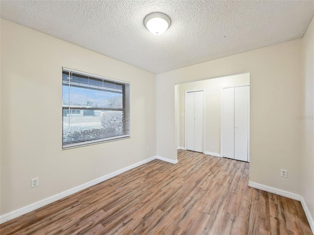 An empty bedroom features light-colored walls, wood-look flooring, a window with blinds, and two closets — 2512 EASTBROOK BOULEVARD, WINTER PARK, FL