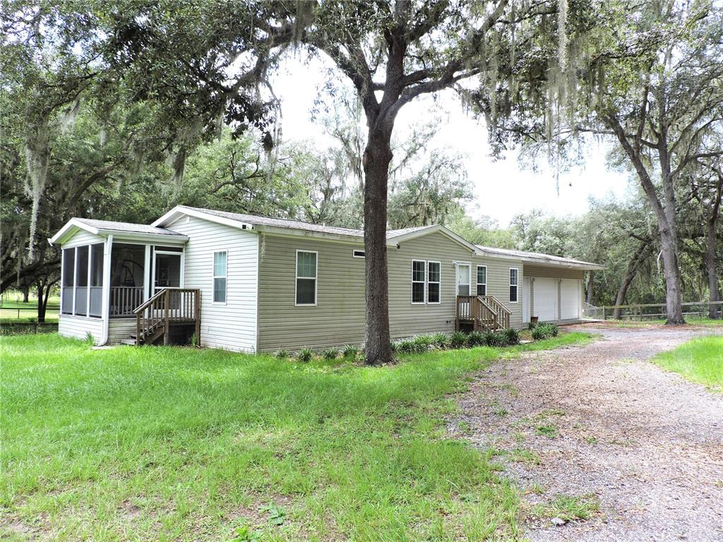A light-colored manufactured home with a screened porch, attached garage, and surrounding oak trees — 29248 WILDLIFE LANE, BROOKSVILLE, FL