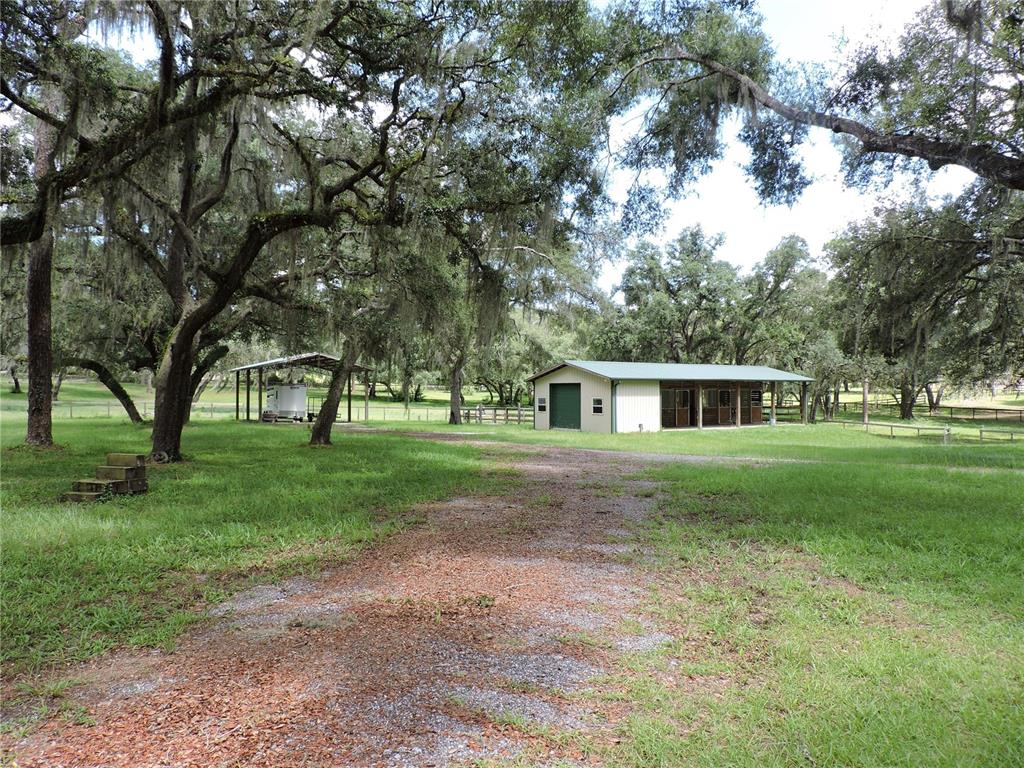A gravel driveway leads to a barn and a covered parking structure under oak trees — 29248 WILDLIFE LANE, BROOKSVILLE, FL