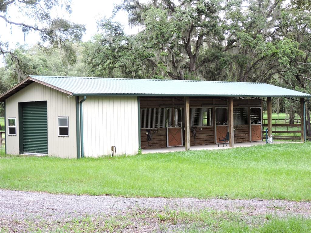 A metal-sided horse barn with a green roof and four individual stalls under an overhang — 29248 WILDLIFE LANE, BROOKSVILLE, FL
