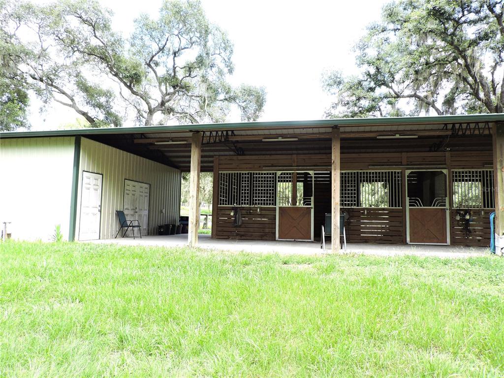 A metal-sided barn features a covered porch with multiple horse stalls and a storage room — 29248 WILDLIFE LANE, BROOKSVILLE, FL