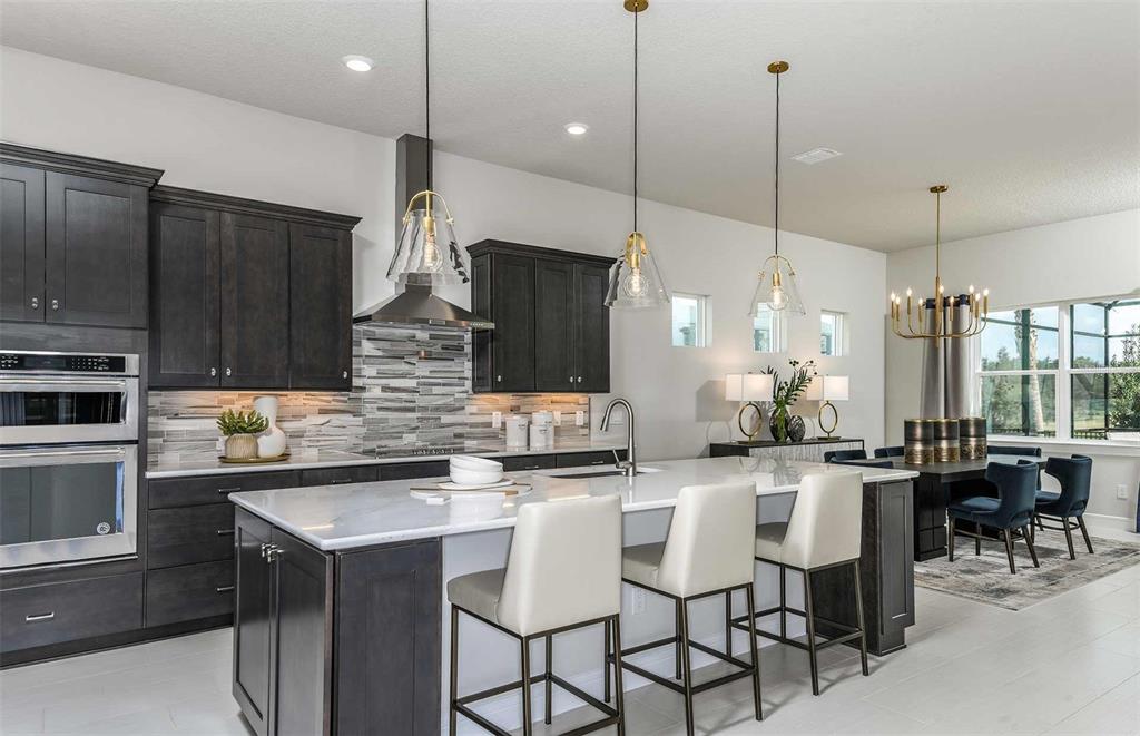 A modern kitchen features dark cabinetry, a large marble-topped island, and three pendant lights — 6390 SW 84TH AVENUE, OCALA, FL