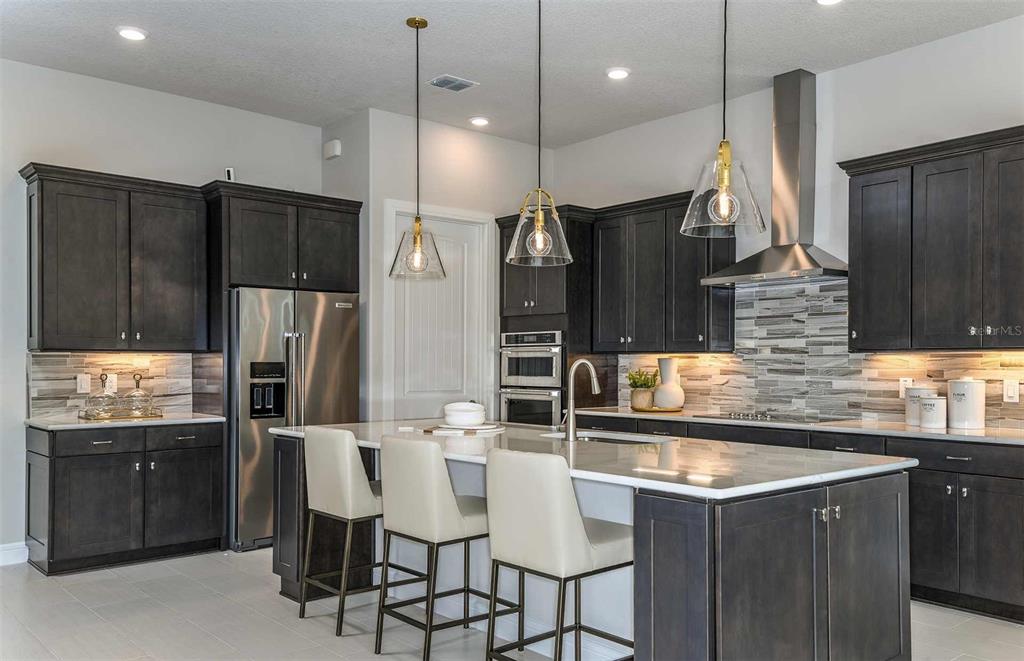 A modern kitchen features dark wood cabinets, stainless steel appliances, and a central island with seating — 6390 SW 84TH AVENUE, OCALA, FL