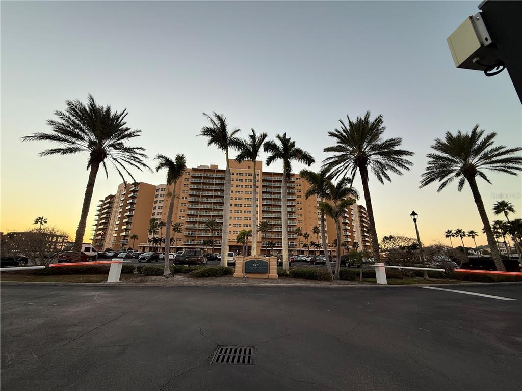 A multi-story tan apartment building stands behind a parking lot with palm trees — 880 MANDALAY AVENUE UNIT C410, CLEARWATER, FL