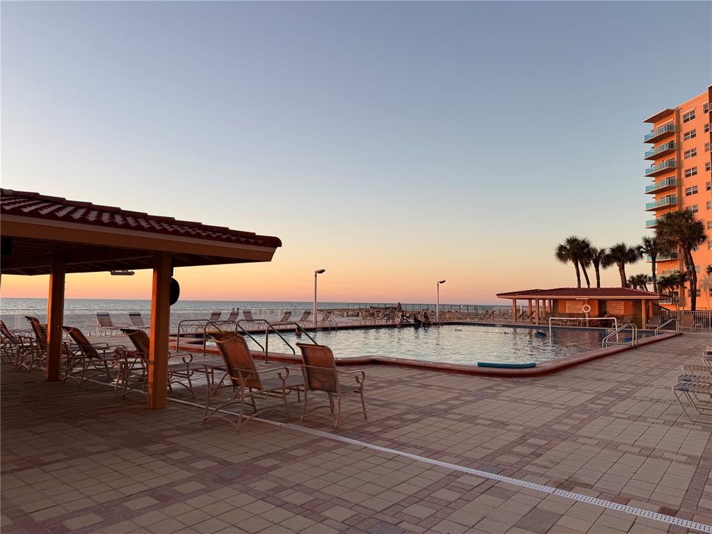 A swimming pool and patio area overlook the ocean at sunset near a tall building — 880 MANDALAY AVENUE UNIT C410, CLEARWATER, FL