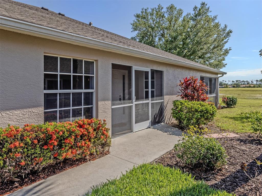 A beige house exterior features a screened entry door, large windows, and landscaped garden beds — 4316 FAIRWAY DRIVE, NORTH PORT, FL