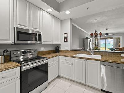 A kitchen with white cabinets, stainless steel appliances, and granite countertops overlooks a living area — 4 Harbour Isle Drive E # 106, Fort Pierce FL 34949, FORT PIERCE, FL