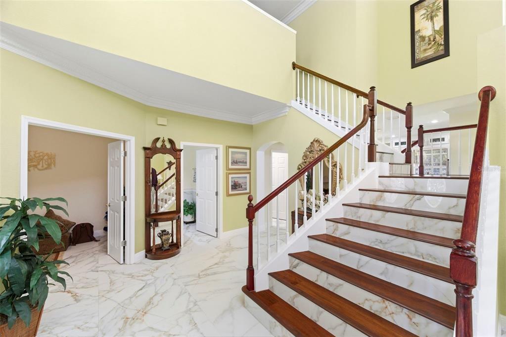 A foyer features a marble-tiled floor, a wooden staircase with white railings, and yellow walls — 9207 MEADOW LANE COURT, TAMPA, FL