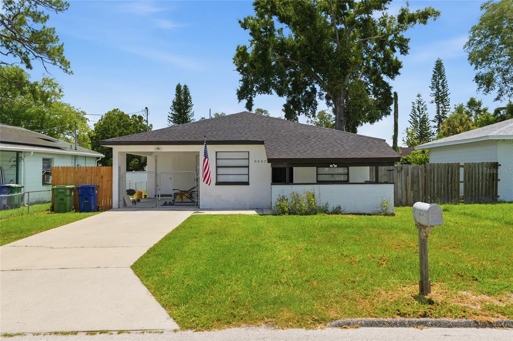 A single-story house with a white exterior, a carport, and a front lawn — 9407 N 21ST STREET, TAMPA, FL