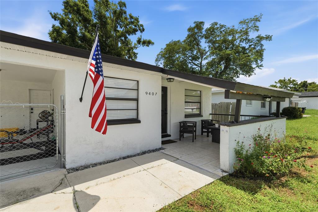 A white house exterior features a front porch, an American flag, and a chain-link fence — 9407 N 21ST STREET, TAMPA, FL