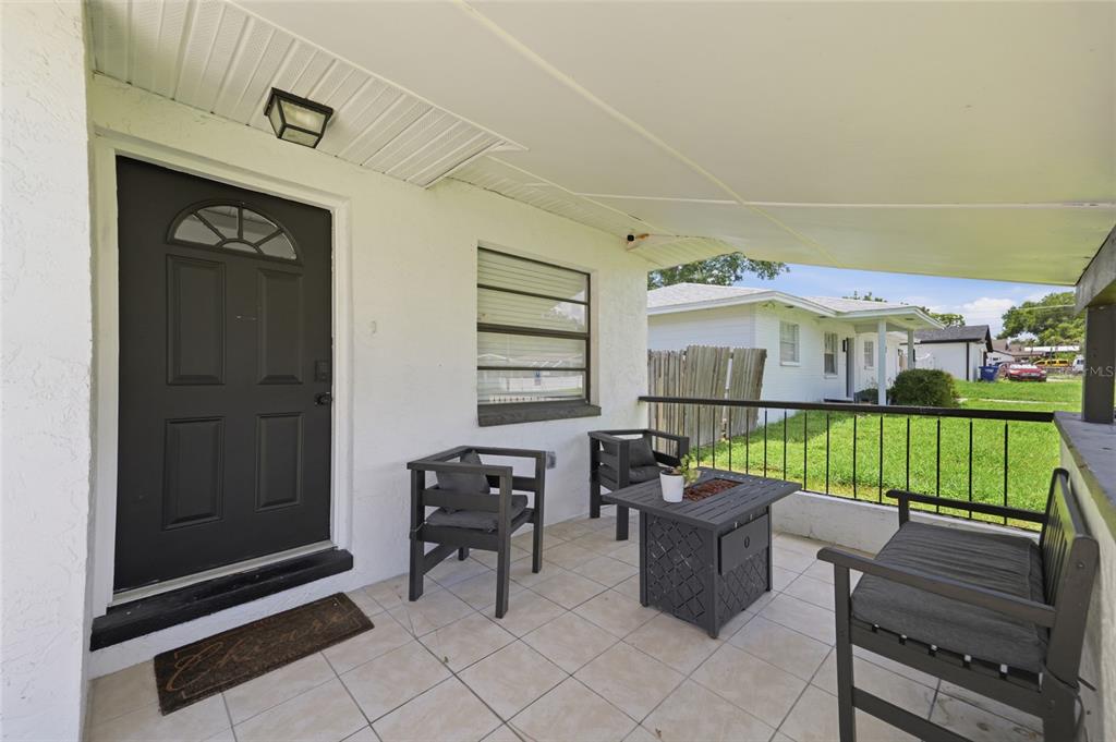 A covered porch features a black front door, tile flooring, and outdoor seating furniture — 9407 N 21ST STREET, TAMPA, FL