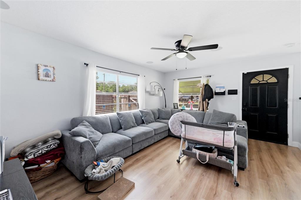 A living room features a gray sectional sofa, light wood flooring, and a black front door — 9407 N 21ST STREET, TAMPA, FL