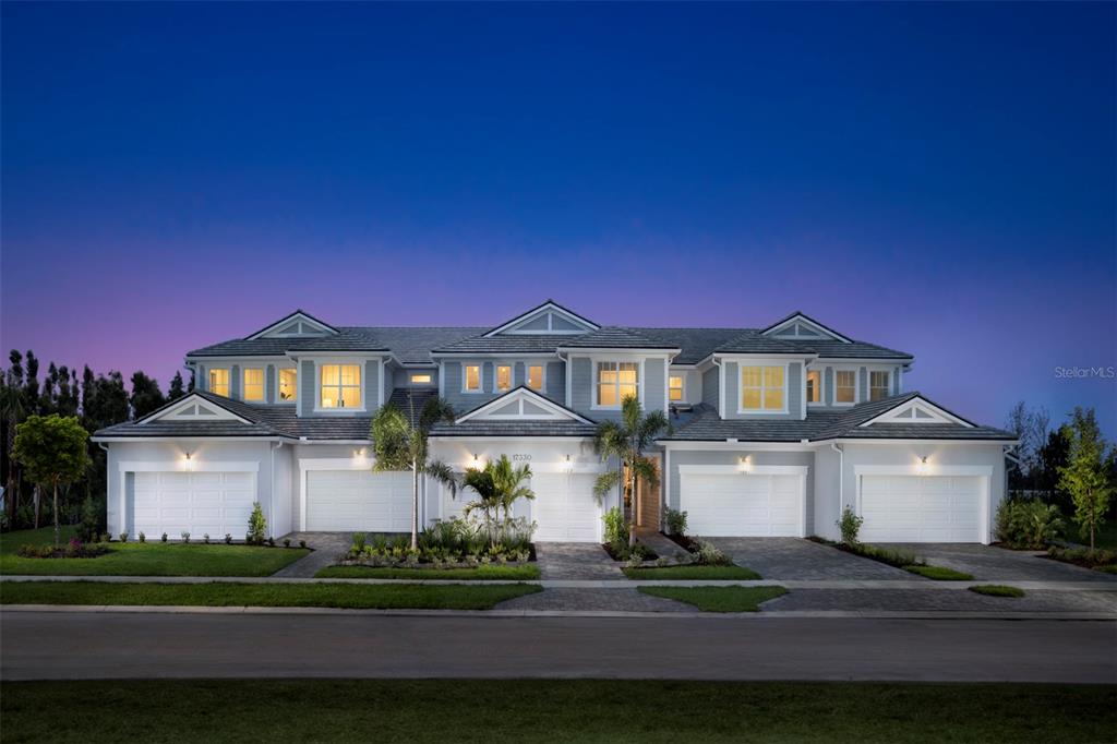 A multi-unit residential building with four garage doors and a paved driveway at dusk — 17405 MOONFLOWER DRIVE UNIT 102, VENICE, FL