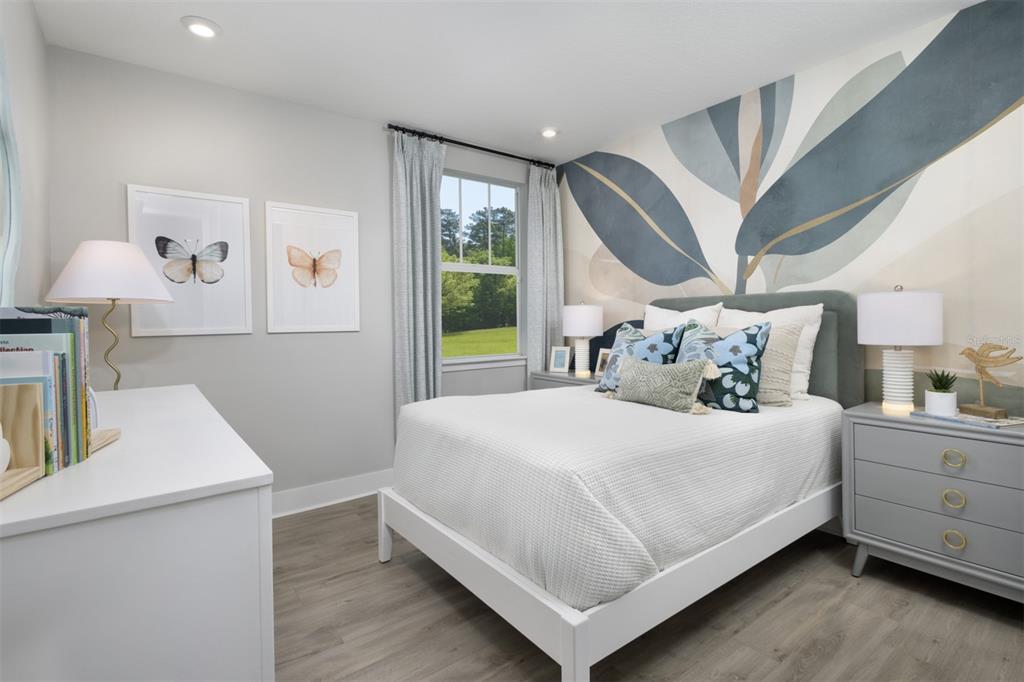 A bedroom features a white bed, a mural wall, gray nightstands, and a window view — 17405 MOONFLOWER DRIVE UNIT 102, VENICE, FL