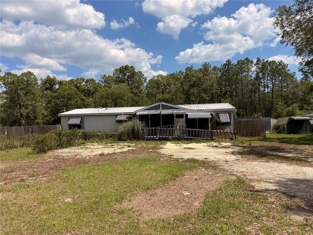 A single-story manufactured home with a metal roof and a wooden ramp entrance — 7561 SE 120TH COURT, MORRISTON, FL