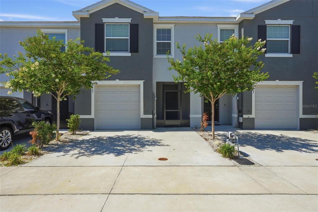 A two-story townhouse exterior features gray siding, white trim, two garage doors, and two trees — 5267 DRAGONFLY DRIVE, WILDWOOD, FL