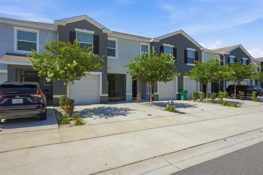 A row of two-story townhomes with attached garages and paved driveways under a blue sky — 5267 DRAGONFLY DRIVE, WILDWOOD, FL