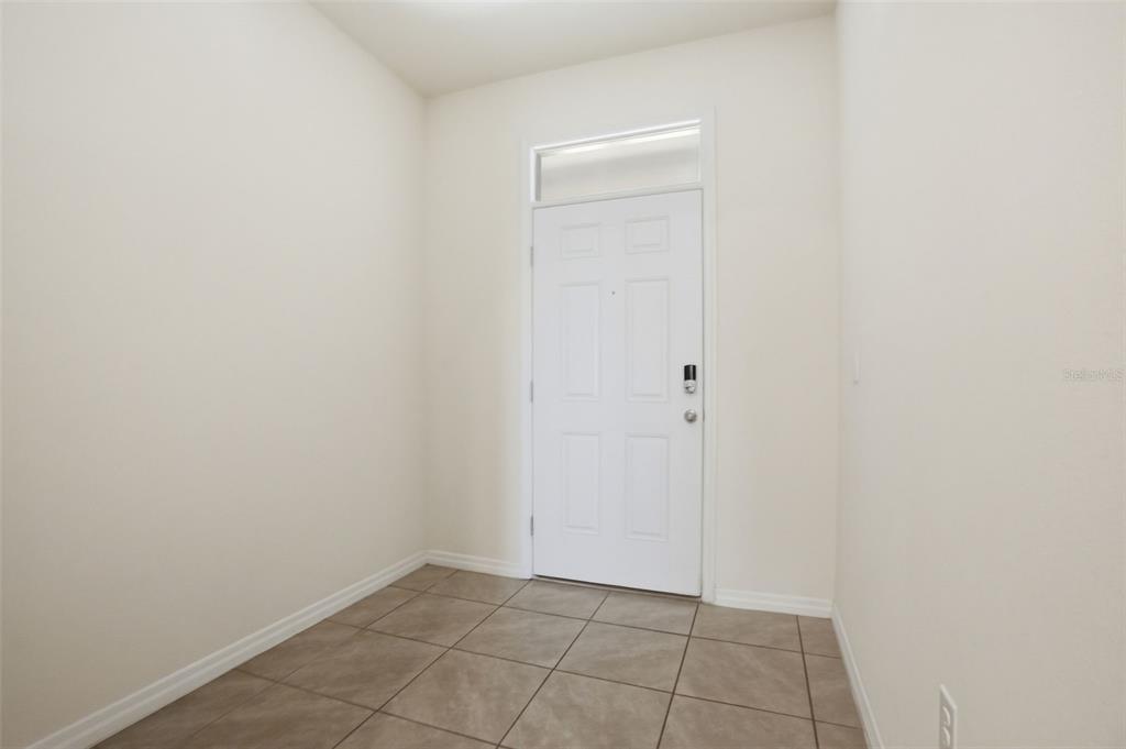 An entryway with beige walls, a white front door, and light brown tile flooring — 5267 DRAGONFLY DRIVE, WILDWOOD, FL