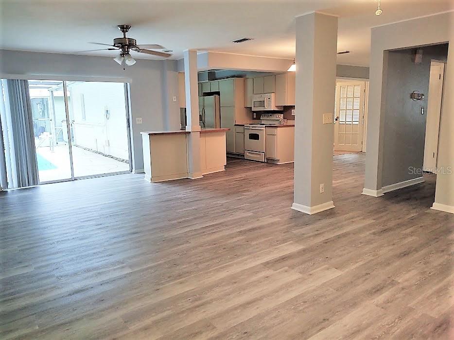 An open-concept living area features light wood-look flooring, a kitchen with white cabinets, and sliding doors — 11003 66TH TERRACE, SEMINOLE, FL