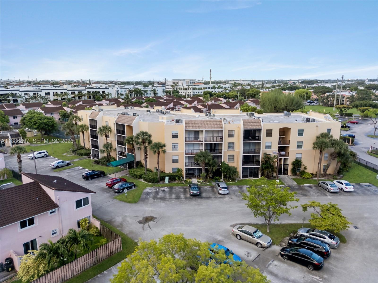 An aerial view shows a multi-story apartment building with a parking lot and surrounding landscaping — 8005 Lake Dr # 404, Doral FL 33166, DORAL, FL
