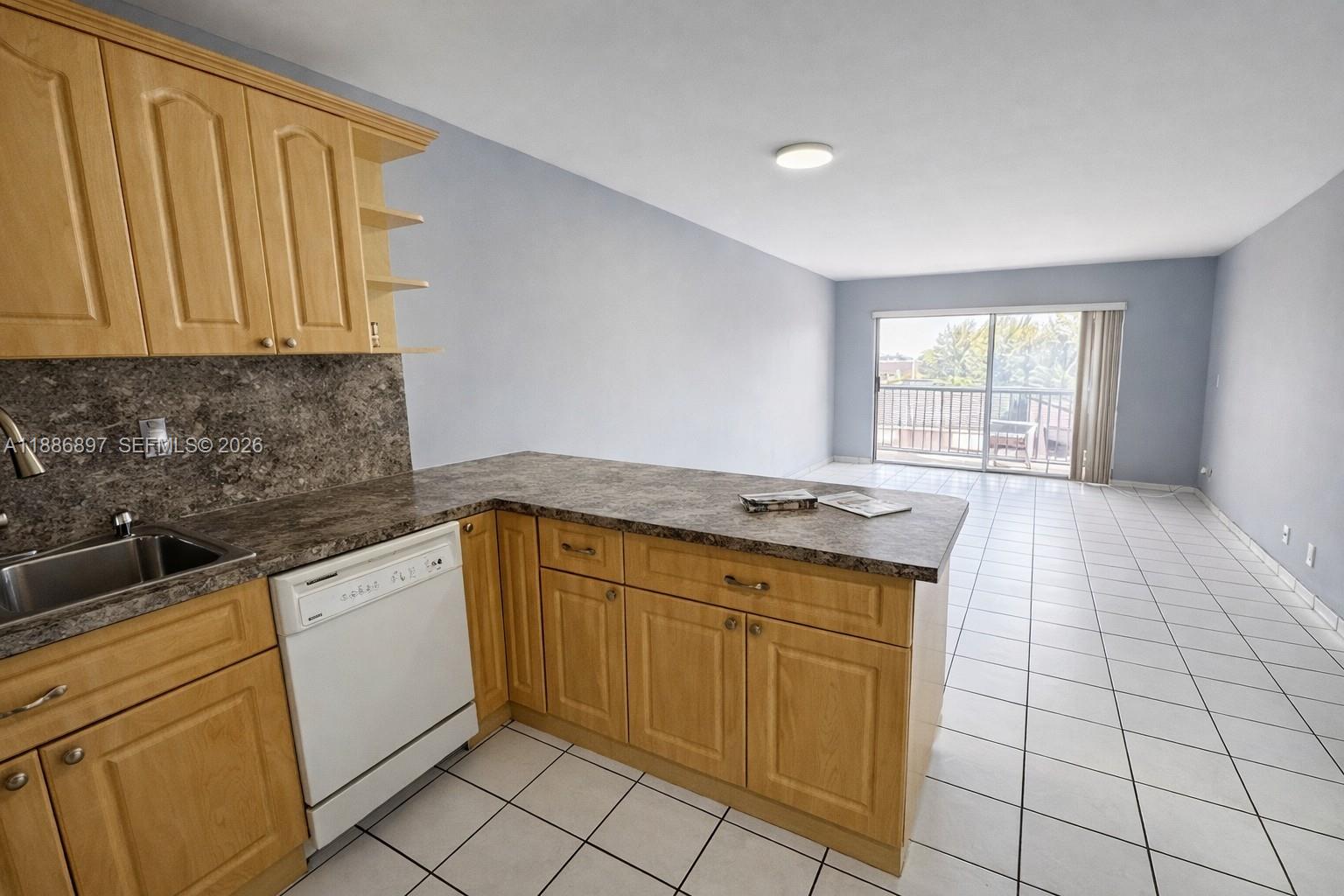 A kitchen with light wood cabinets and stone-look countertops opens into a tiled living area — 8005 Lake Dr # 404, Doral FL 33166, DORAL, FL