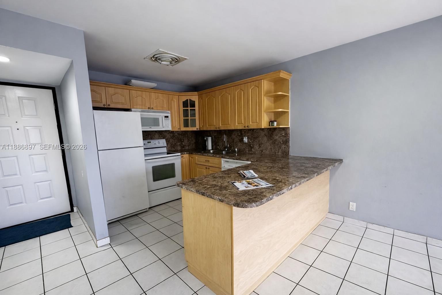 A kitchen features light wood cabinets, brown laminate countertops, white appliances, and white tile flooring — 8005 Lake Dr # 404, Doral FL 33166, DORAL, FL