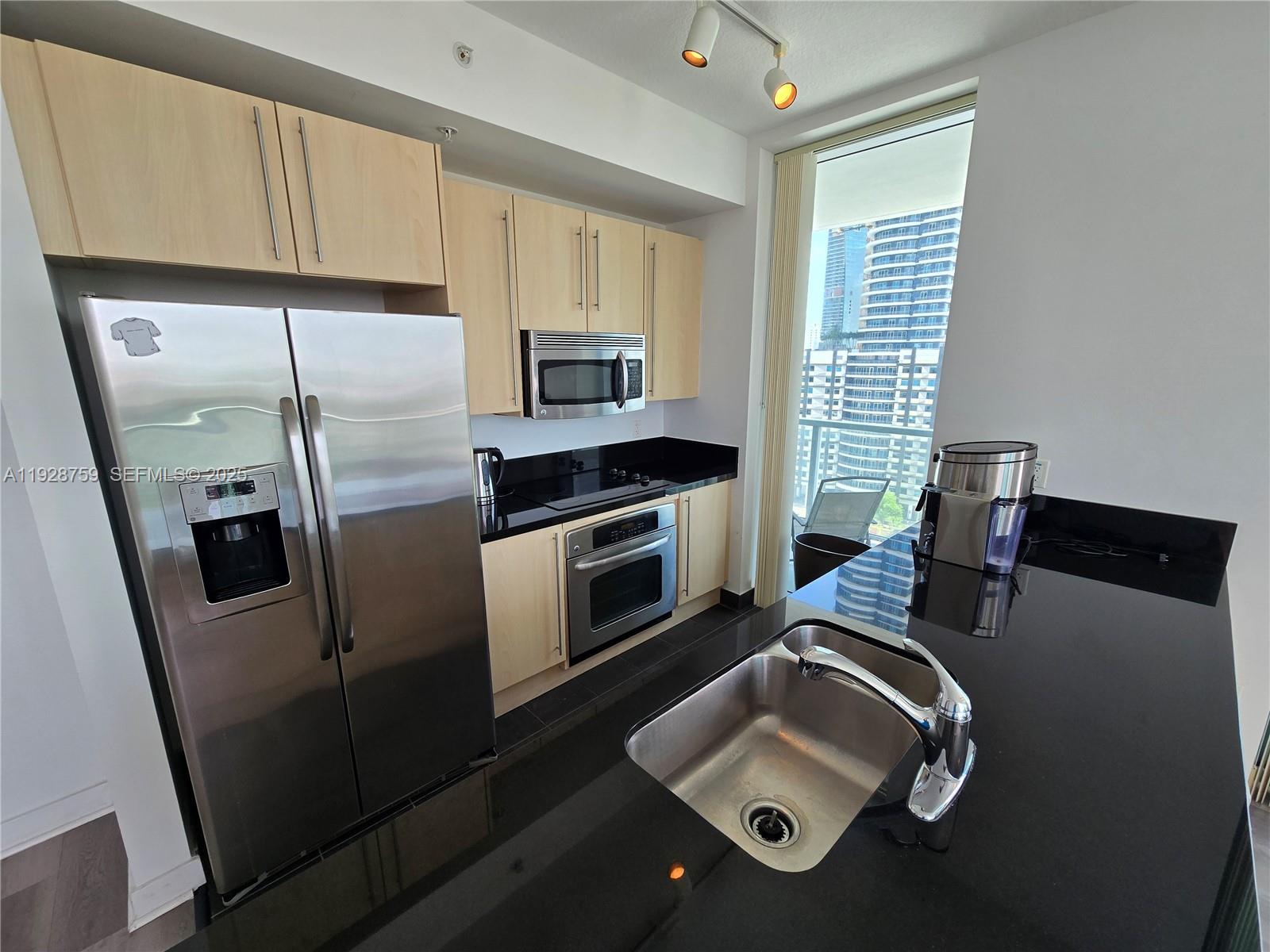 A modern kitchen features light wood cabinets, black countertops, stainless steel appliances, and city views — 79 SW 12th St, Miami FL 33130, MIAMI, FL
