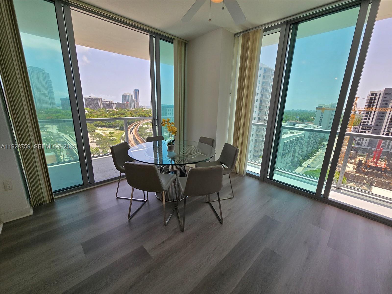 A dining area with a glass table and chairs sits between floor-to-ceiling windows overlooking cityscapes — 79 SW 12th St, Miami FL 33130, MIAMI, FL