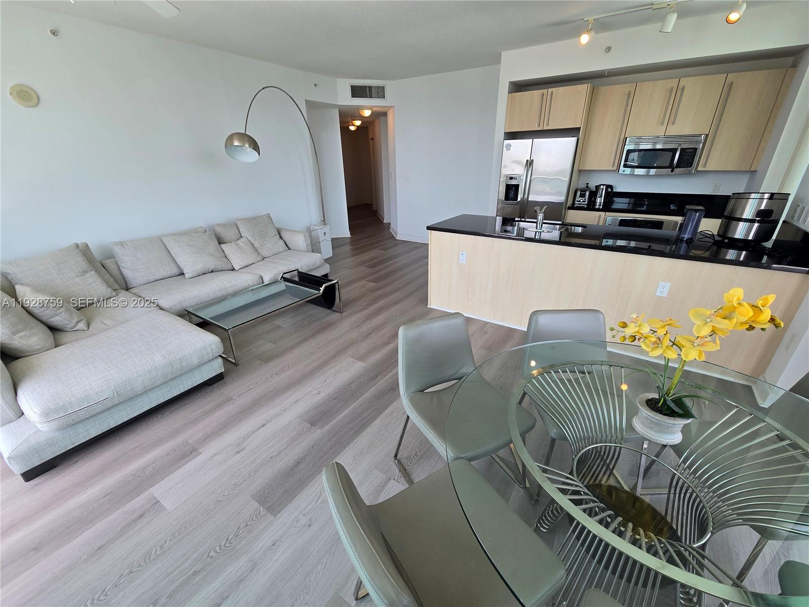 An open-concept living and dining area features light wood floors, a sectional sofa, and kitchen — 79 SW 12th St, Miami FL 33130, MIAMI, FL