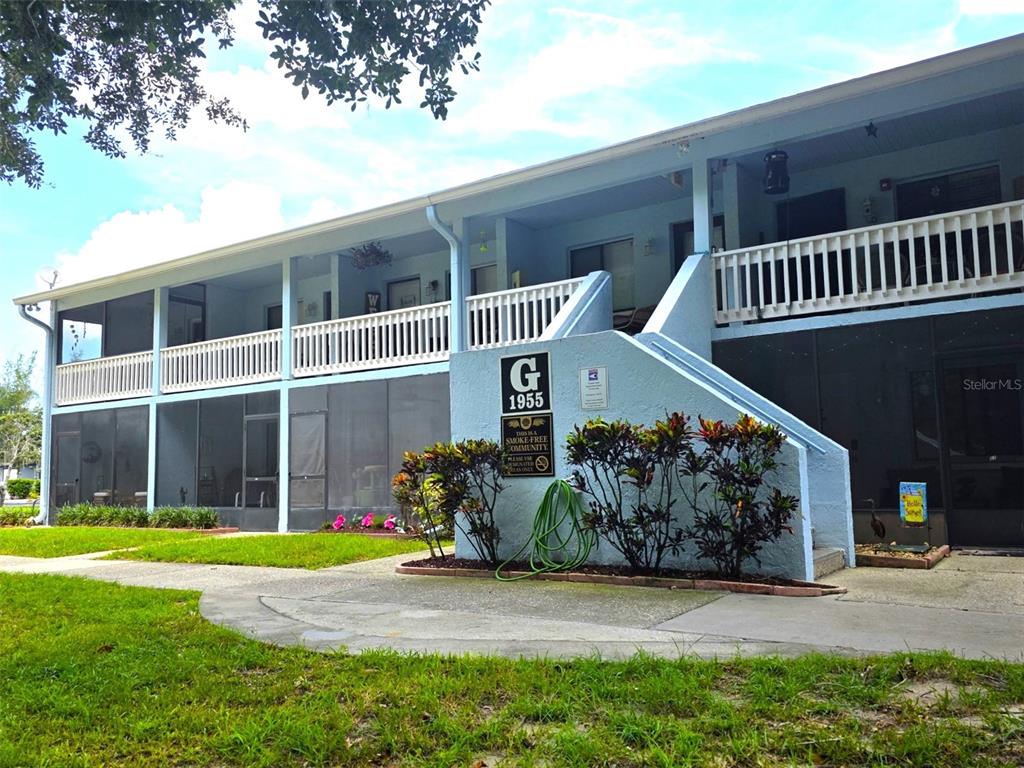 A two-story apartment building exterior features a blue facade, screened-in porches, and a concrete staircase — 1955 ABRICO DRIVE UNIT G16, LUTZ, FL
