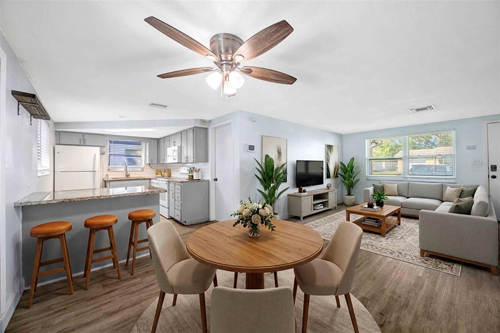 An open-concept living and dining area features a kitchen with bar seating and wood flooring — 9040 LUNAR LANE, PORT RICHEY, FL