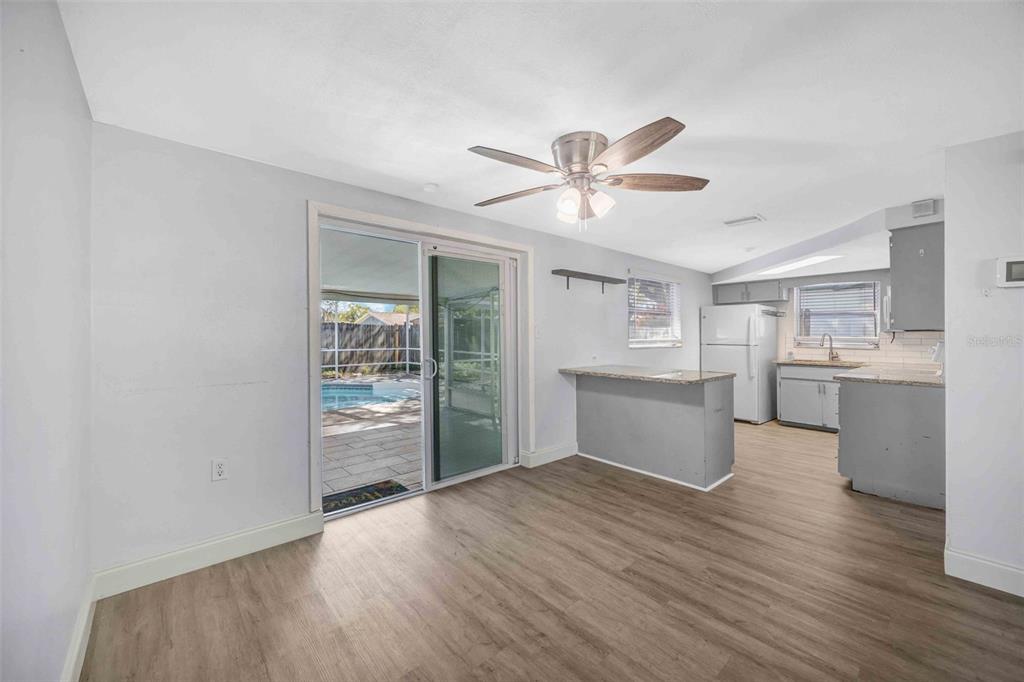 An open-concept kitchen and dining area with wood-look flooring and a sliding door to a pool — 9040 LUNAR LANE, PORT RICHEY, FL